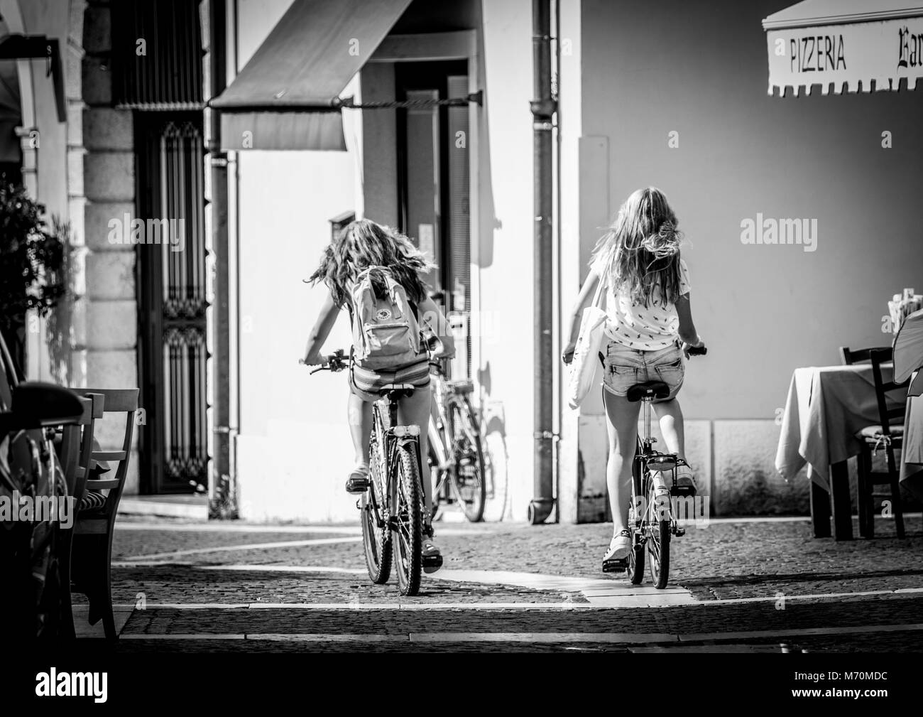 Dos muchachas jóvenes en bicicleta por una calle empedrada entre la calle restaurantes en Bardolino Lago de Garda en Italia Foto de stock