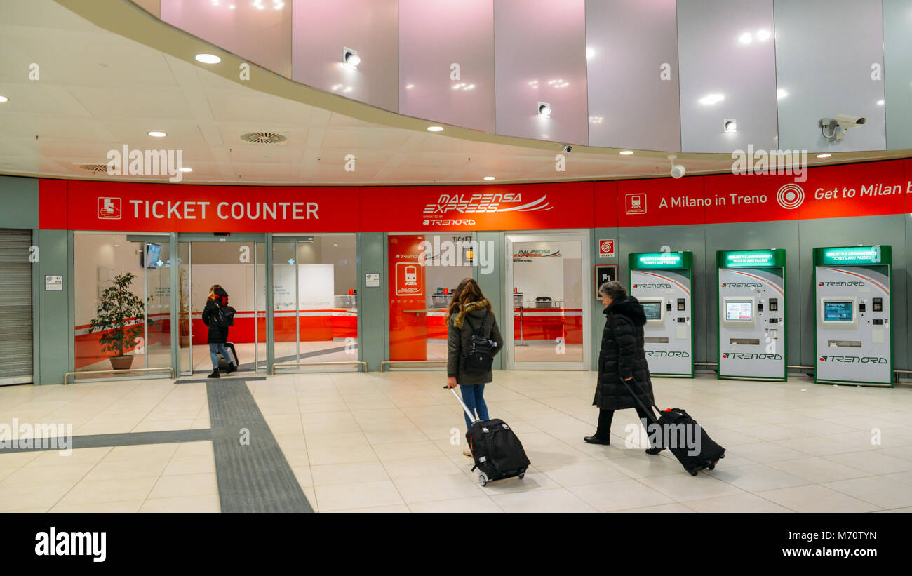 Los pasajeros con equipaje de mano a pie pasar el mostrador de venta de  boletos para el Malpensa Express, un servicio de tren rápido hasta Cardona,  y la Estación Central de Milán