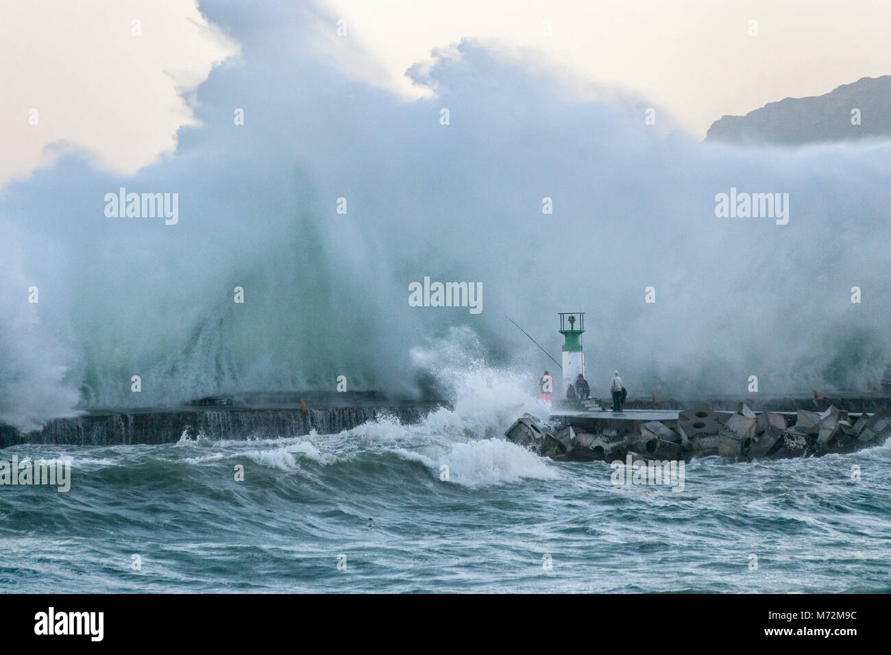 Los pescadores sorteando enormes olas que pueden verse aquí reventándose contra el rompeolas de Kalk Bay Harbour en Cape Town, Sudáfrica. Foto de stock