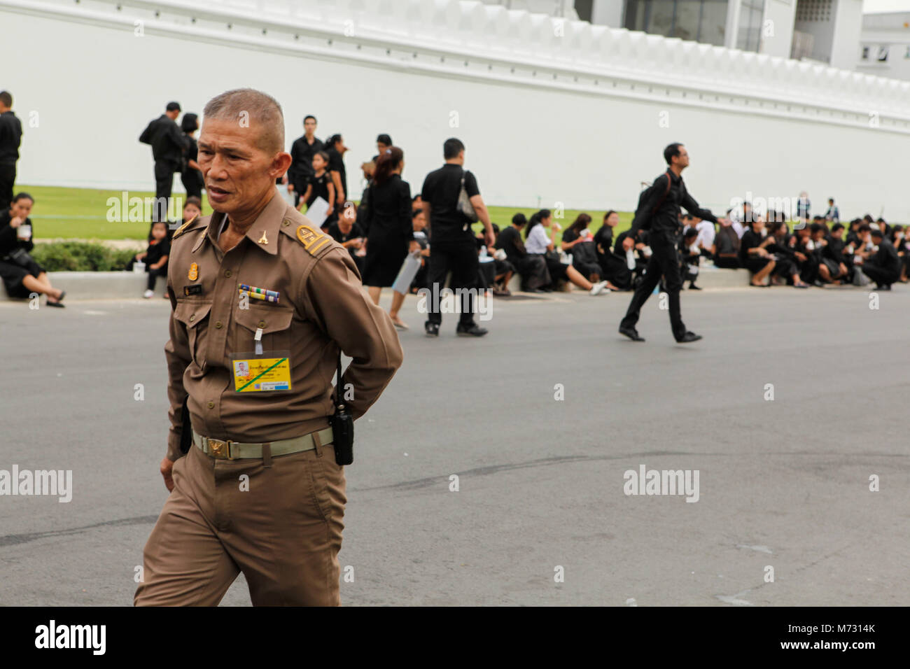 Un oficial del ejército tailandés camina en la calle fuera de los muros blancos de la Grand Palace de Bangkok, entre la gente de luto vistiendo ropa negra Foto de stock
