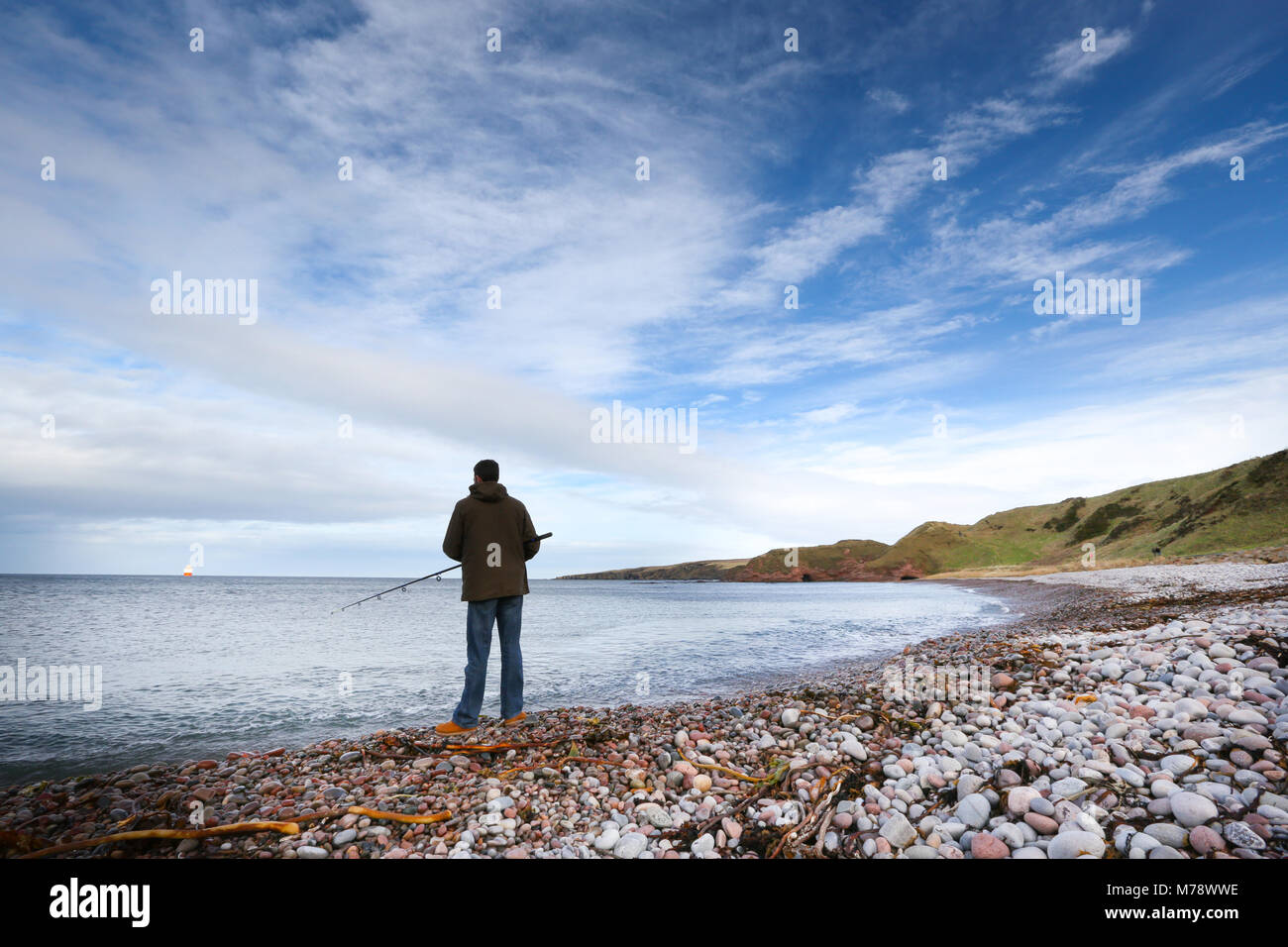 Hombre que pesca en el Mar del Norte desde la culebrilla en Aberdour nueva playa en Aberdeenshire, Escocia, Reino Unido Foto de stock