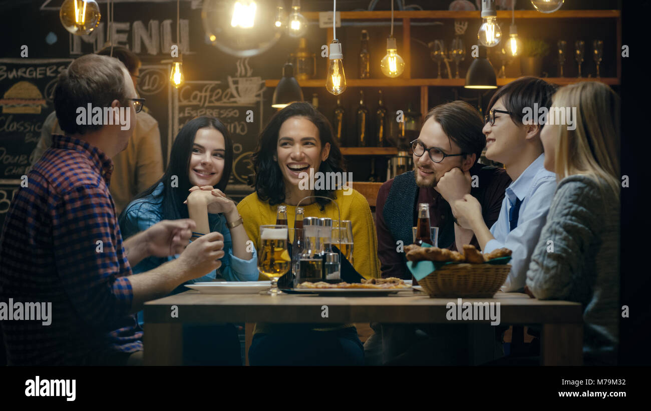 Diversos grupos de jóvenes se divierten en Bar, conversar, contar cuentos y chistes. Beben distintas bebidas. Se encuentra en la elegante Hipster Foto de stock