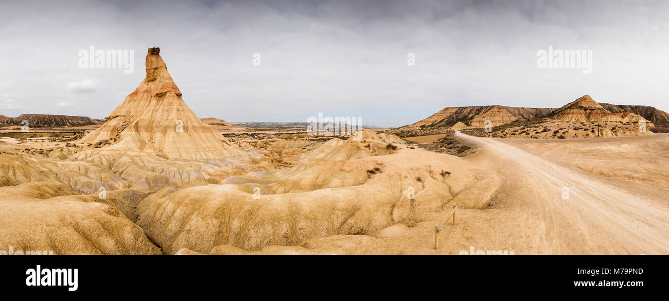 Imagen panorámica de Castildetierra 'castillo de la tierra', un natural de torre en el desierto de Las Bardenas Reales, con nubes oscuras y la pista que cruza el parque Foto de stock
