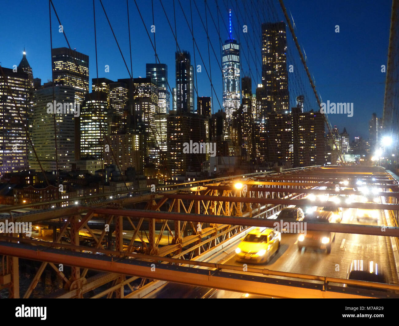 Puente de Brooklyn en Nueva York, construido en 1883, con tráfico de vehículos cruzando durante el crepúsculo y el centro de Manhattan, torres de oficinas Foto de stock
