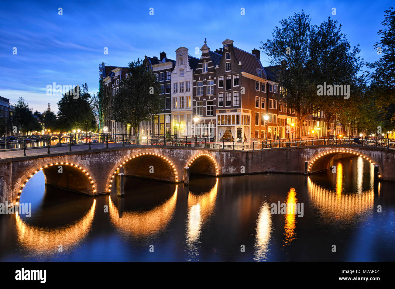 Escena nocturna en un canal, con edificios tradicionales y un puente de arco en Ámsterdam, Países Bajos Foto de stock