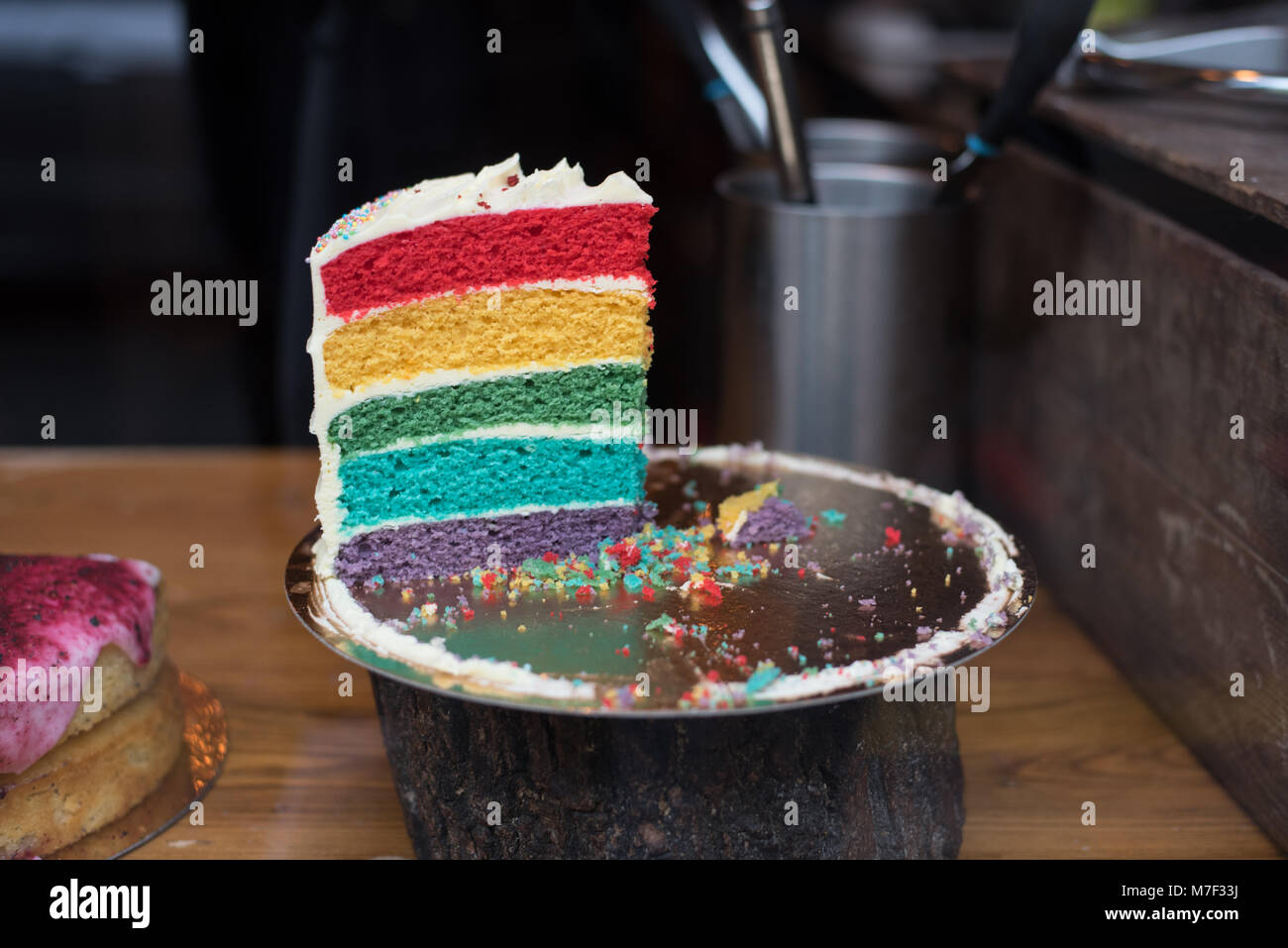 Yummy buscando rebanada de rainbow bizcocho con glaseado blanco sobre un pastel de stand con fondo oscuro Foto de stock