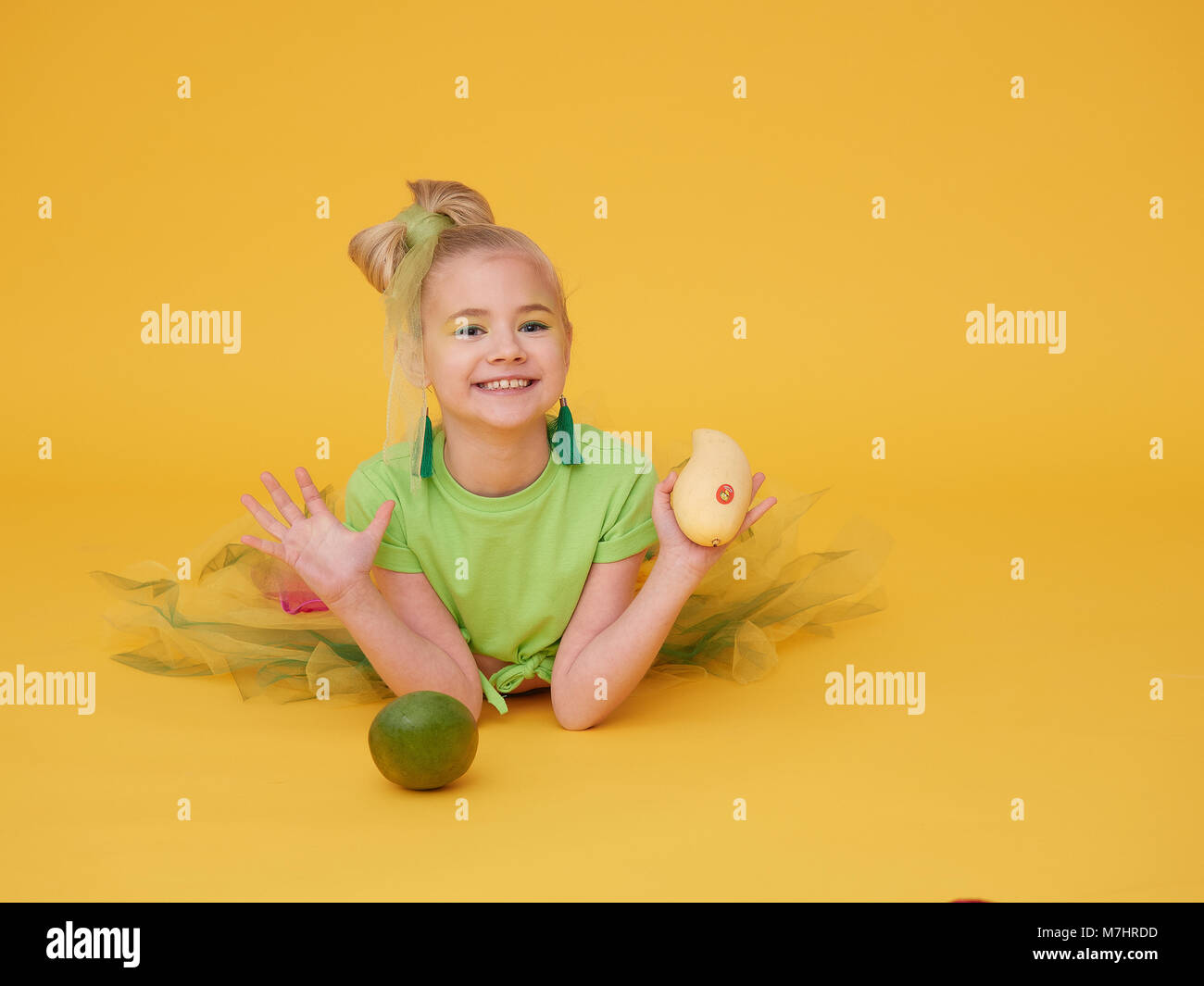 El rubio niña viste una camiseta de color verde claro y una falda de  colores brillantes.sostener al bebé sujetando el mango, frutos de  diferentes variedades Fotografía de stock - Alamy