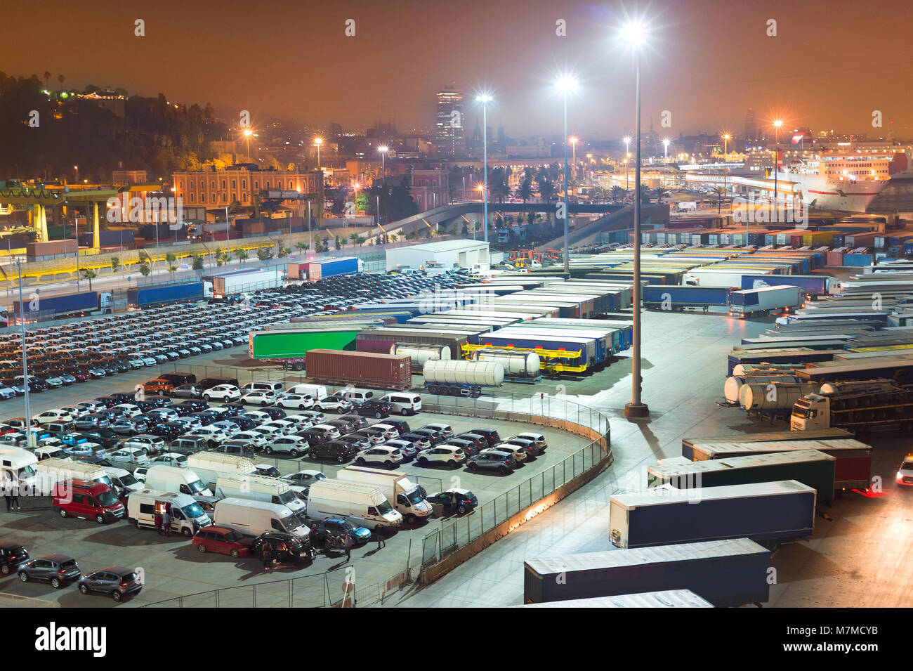 Automóviles y camiones en un gran espacio de aparcamiento en el puerto industrial de Barcelona por la noche. España Foto de stock