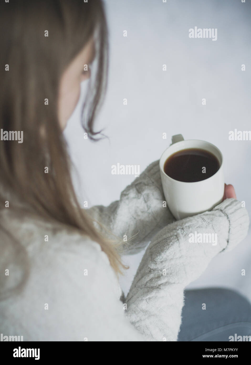 Una a través de la captura debe de una joven chica sujetando una taza caliente de café negro en sus manos mientras sentado solo y sobre un fondo blanco. Foto de stock