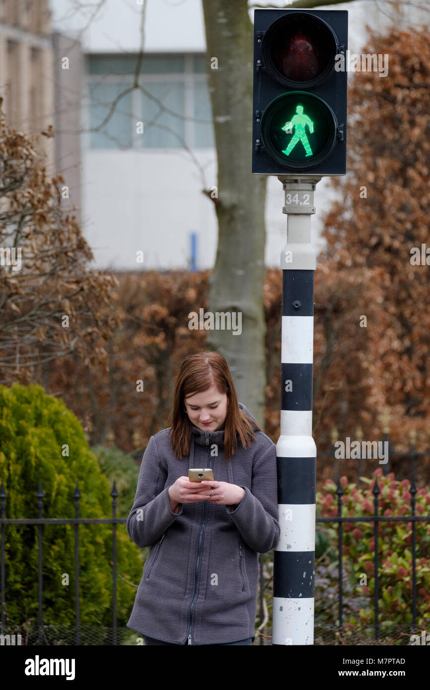 Joven Mujer espera en un semáforo que está en verde, pero no presta atención al tráfico porque ella mira a su teléfono móvil. Foto de stock
