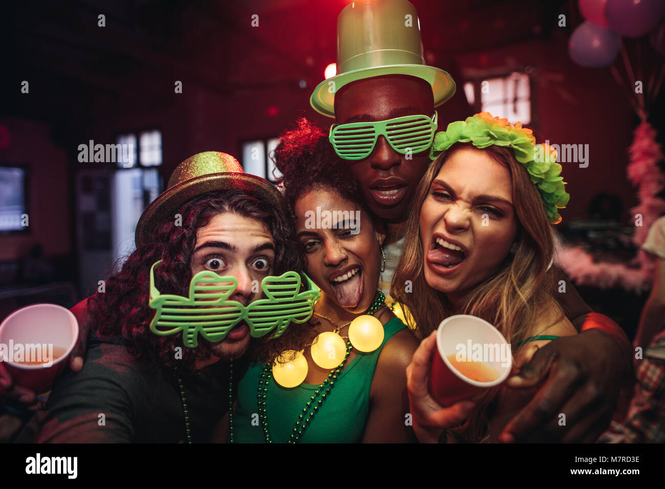Crazy jóvenes amigos disfrutando de una fiesta en el pub. Hombres y mujeres en el trébol verde parte de anteojos y sombrero de duende en el club nocturno. La gente celebrándolo St.Patri Foto de stock