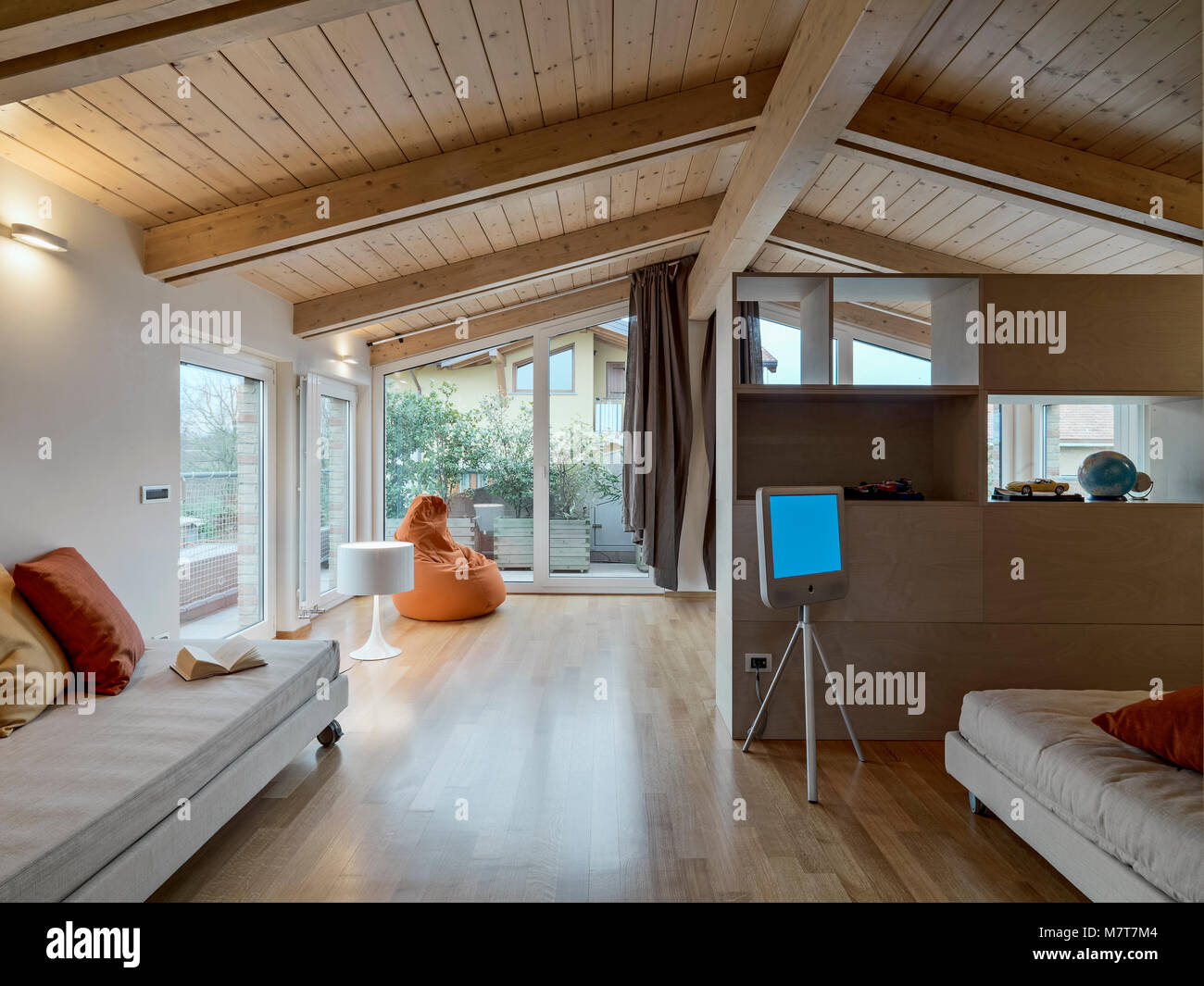 Fotos de un interior moderno con ático en primer plano un sofá de tela, en el fondo de un sillón naranja, el techo y el piso están hechos de madera Foto de stock