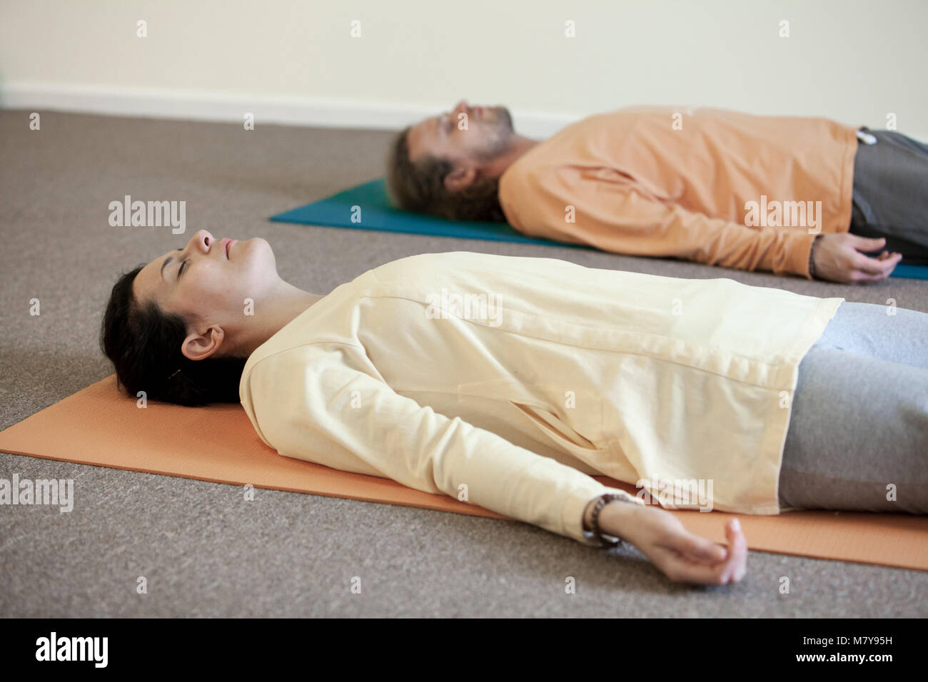 Dos jóvenes practicando la relajación también llamado yoga nidra. En shavasana tendido sobre su espalda, sobre sus colchonetas para yoga en el yoga clases sueltas en el interior LI Foto de stock