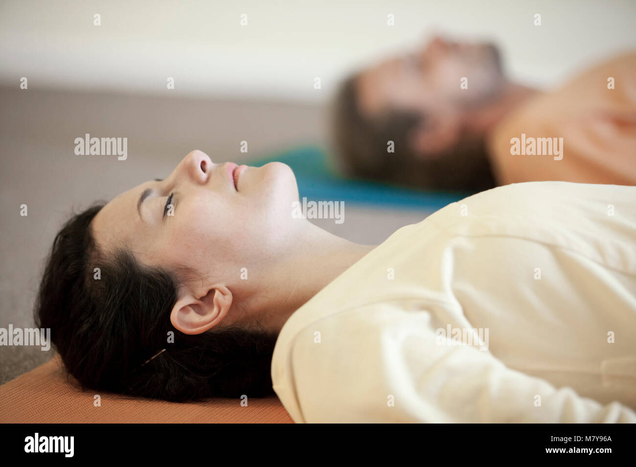 Dos jóvenes practicando la relajación también llamado yoga nidra. En shavasana tendido sobre su espalda, sobre sus colchonetas para yoga en el yoga clases sueltas en el interior LI Foto de stock