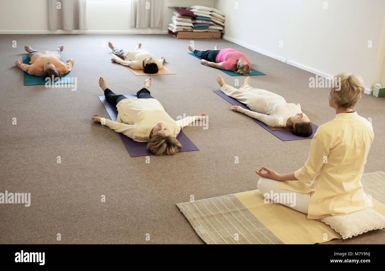 Los jóvenes practicando la relajación también llamado yoga nidra. Guiado por un instructor de yoga certificado hembra poniendo en shavasana sobre sus espaldas en la estera del yoga Foto de stock