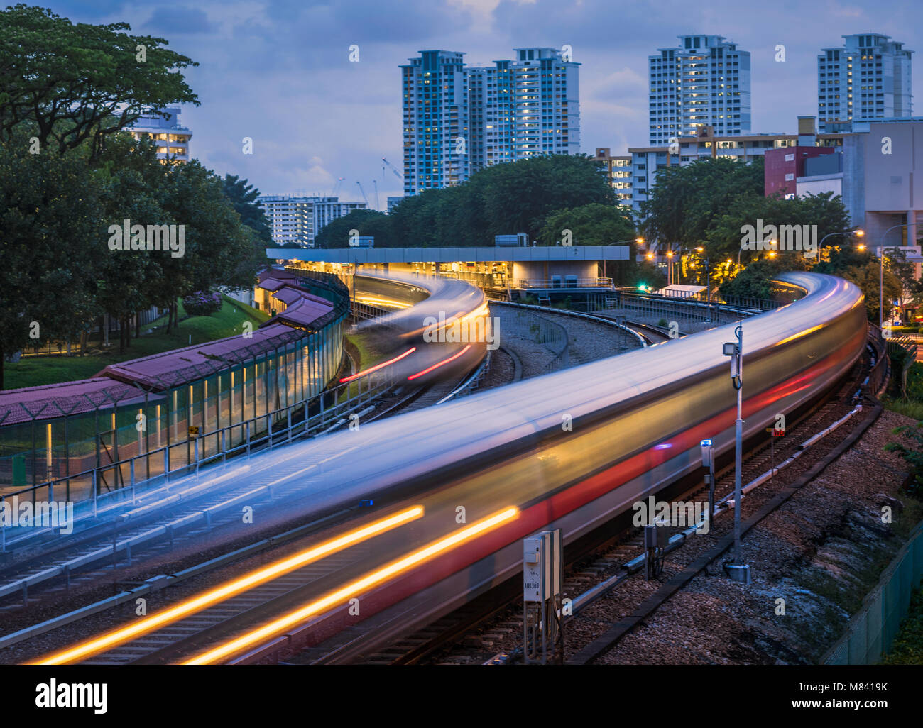 Mass Rapid Transit (MRT) pasando Ang Mo Kio estación en Singapur. La imagen fue tomada después de la puesta de sol y dispone de trenes que cruzan con desenfoque de movimiento. Foto de stock