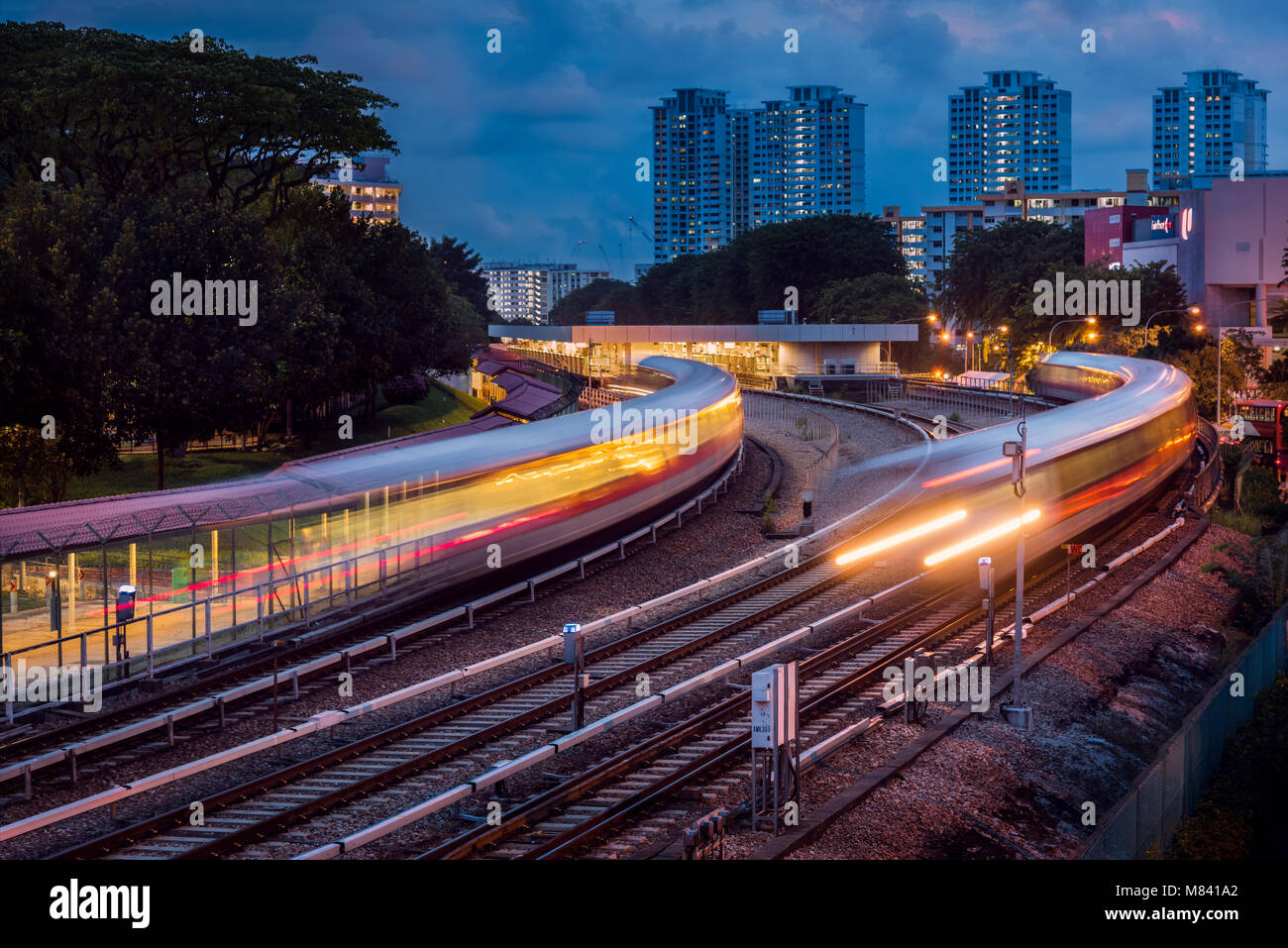 Mass Rapid Transit (MRT) pasando Ang Mo Kio estación en Singapur. La imagen fue tomada después de la puesta de sol y dispone de trenes que cruzan con desenfoque de movimiento. Foto de stock