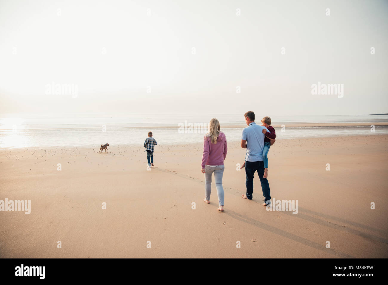 Vista trasera de familia con dos hijos andando hacia el borde del agua mientras se encuentra de vacaciones. Foto de stock