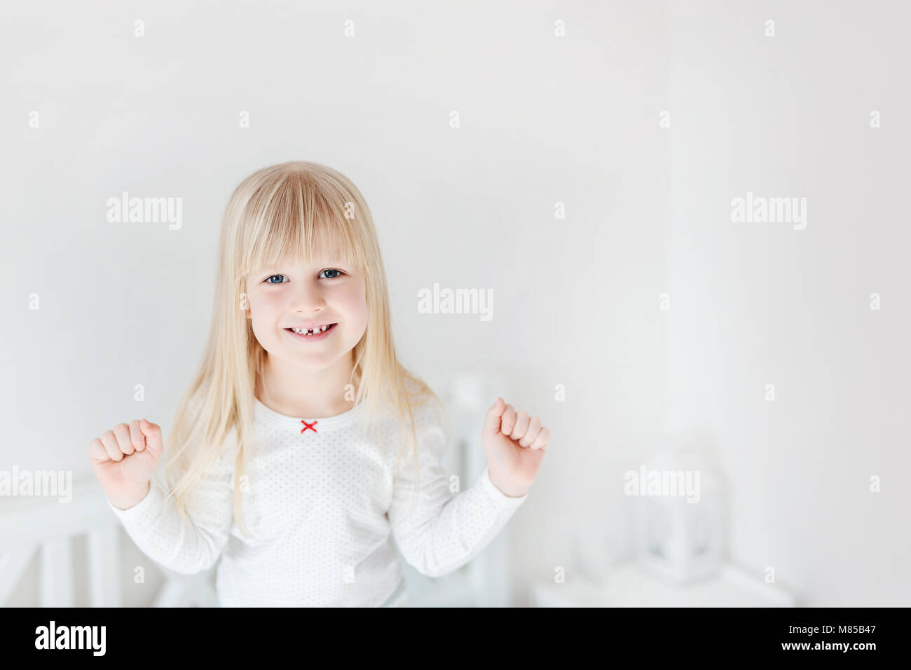 Retrato de poco lindo chica de pie sobre la cama. Adorable niño sonriente. Rubio kid levantando los puños. Los niños victoria o éxito concepto Foto de stock