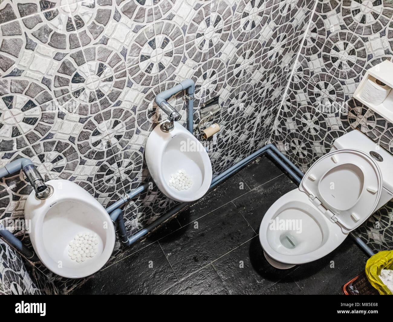 Una extraña combinación de dos extraños urinarios y un inodoro en un baño público en Hoi An, Vietnam Foto de stock