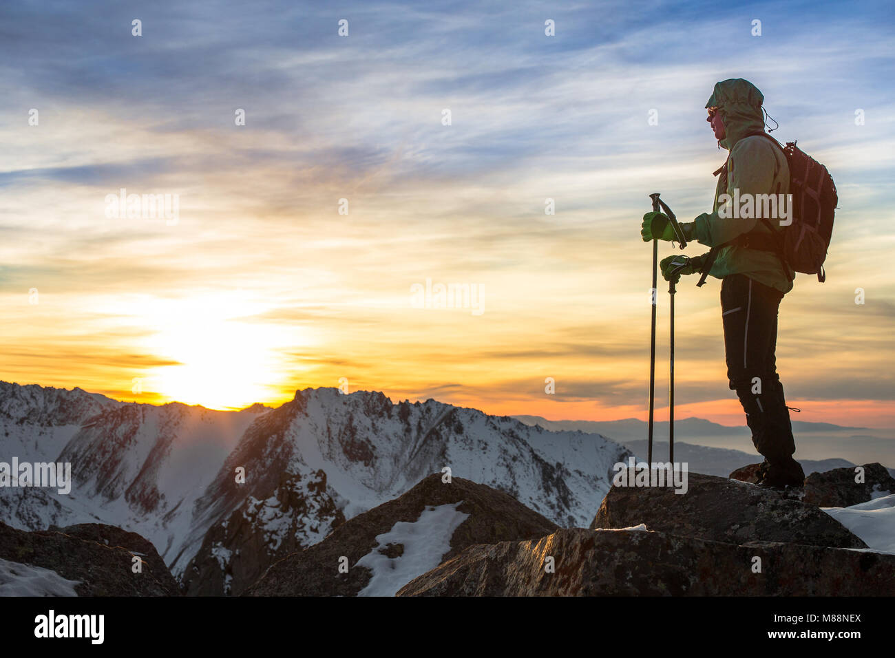 Un hombre se encuentra en la parte superior de la cumbre rocosa viendo sorprendente colorido atardecer. Trans-Ili Alatau de montañas. Región de Almaty. Kazajstán. Foto de stock