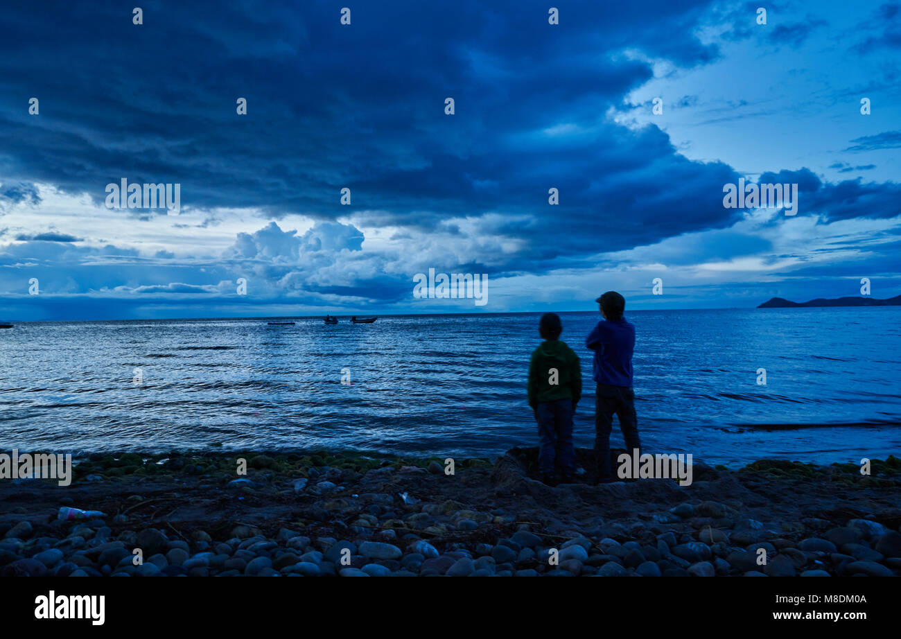 Dos chicos de pie al lado del lago, mirando a ver, vista trasera, Copacabana, Oruro, Bolivia, América del Sur Foto de stock