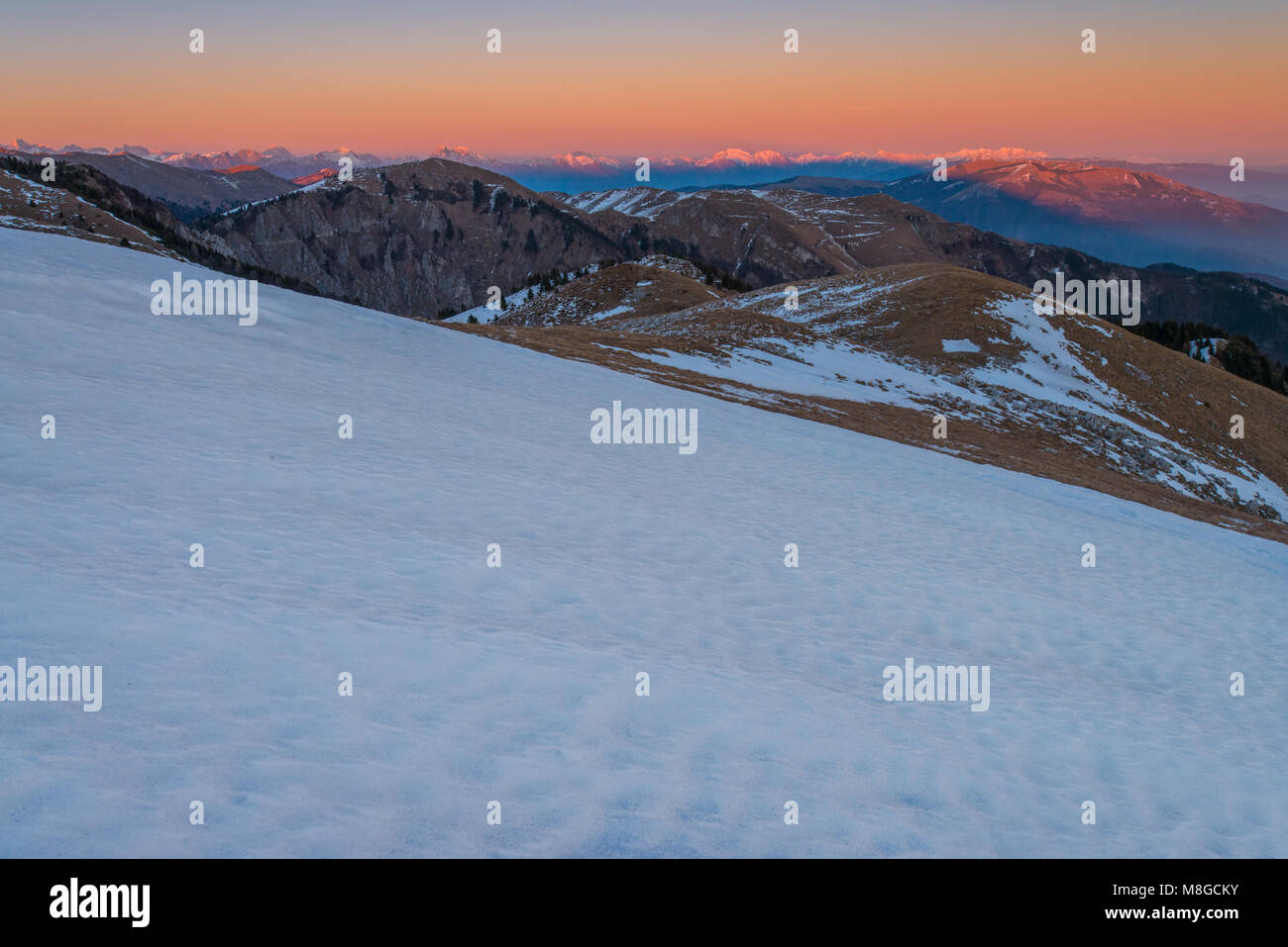 Pinturas alpenglow majestuosas montañas y nubes al atardecer, mirando hacia el valle. La nieve fresca convierte las cimas y laderas de color blanco, la primera nieve del invierno. Foto de stock