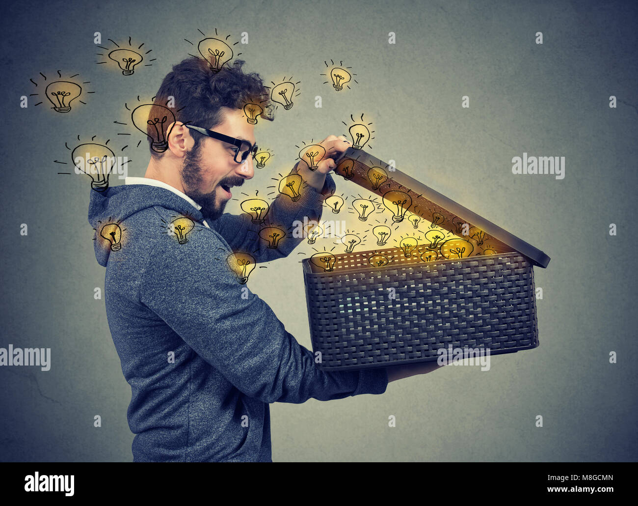 Feliz el hombre sorprendido abriendo una caja con muchas lámparas de luz brillante volador Foto de stock