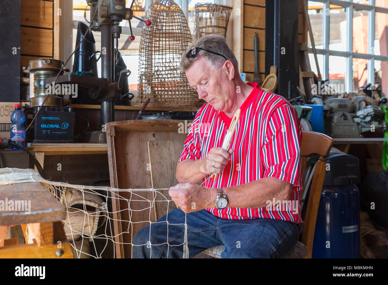 Hombre en traje tradicional holandés arreglando las redes de pesca en el taller Fotografía de Hombre en traje tradicional holandés arreglando las redes de pesca en el taller Fotografía de