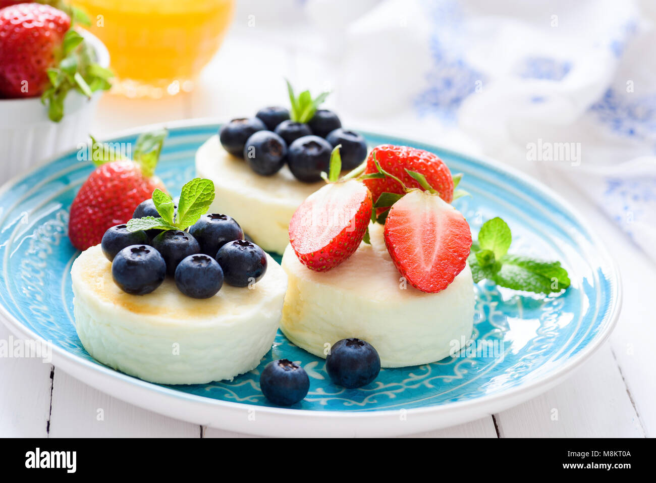 Mini tartas de queso con fresas frescas y arándanos sobre placa azul, acercamiento. Tortitas, queso cottage Syrniki Foto de stock