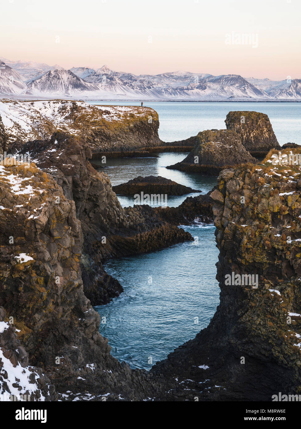 Visión idílica de formaciones rocosas en el mar contra las montañas durante el invierno Foto de stock