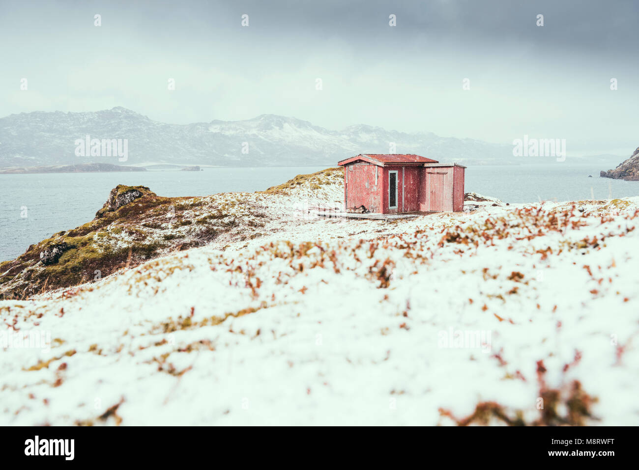 Cabaña junto al lago contra las montañas durante el invierno Foto de stock