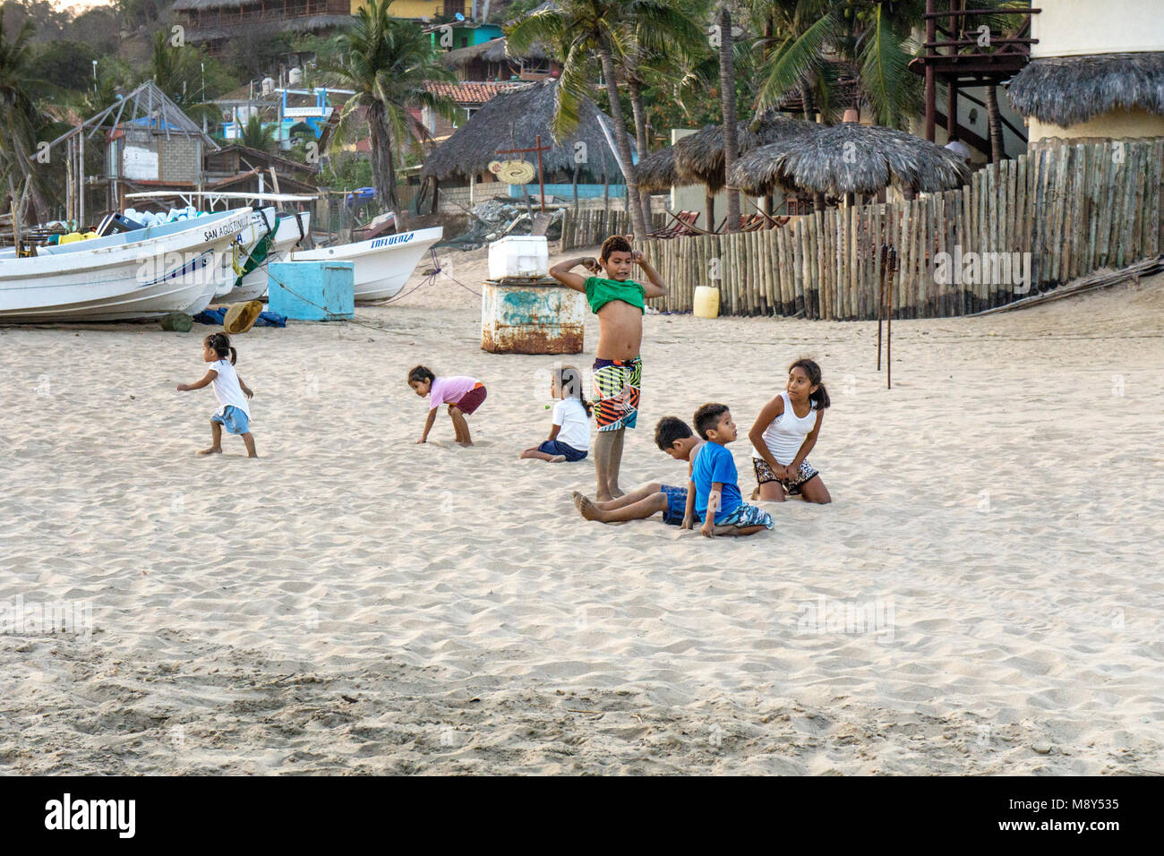 Grupo de niños mexicanos, desde niños pequeños a las interpolaciones juegan en la arena cerca de varadas barcas de pesca, posiblemente, todos parte de la extensa familia de pescadores relacionadas Foto de stock