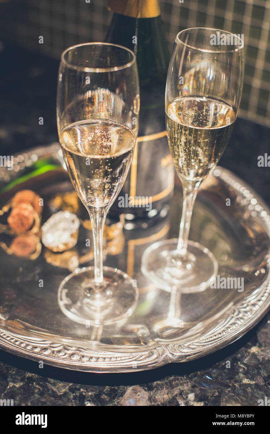 Dos copas de champaña o vino espumoso en una bandeja de plata con el corcho y la botella en el fondo Foto de stock