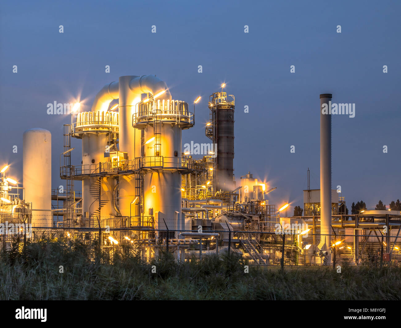 Escena nocturna de los detalles de una planta industrial química pesada con mazework de tubos en penumbra Foto de stock