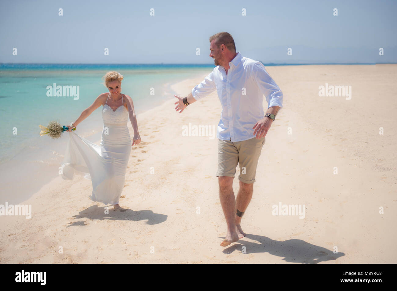 Hermosa pareja caminando juntos en un paraíso tropical en la playa en el día de la boda en bata vestido blanco con vista al mar Foto de stock