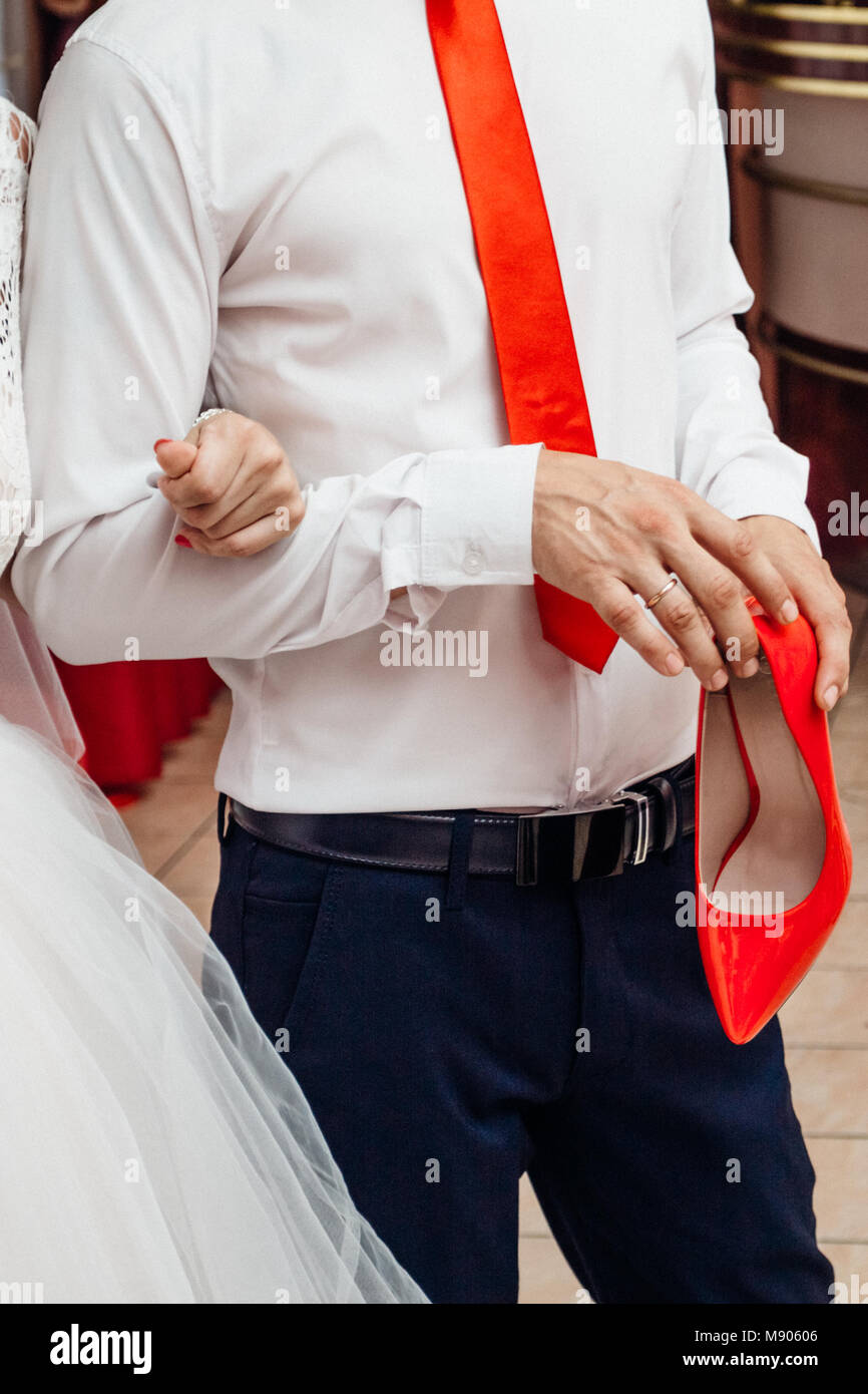 El novio en una camisa blanca con una corbata roja es la celebración de un  zapato rojo de la novia Fotografía de stock - Alamy