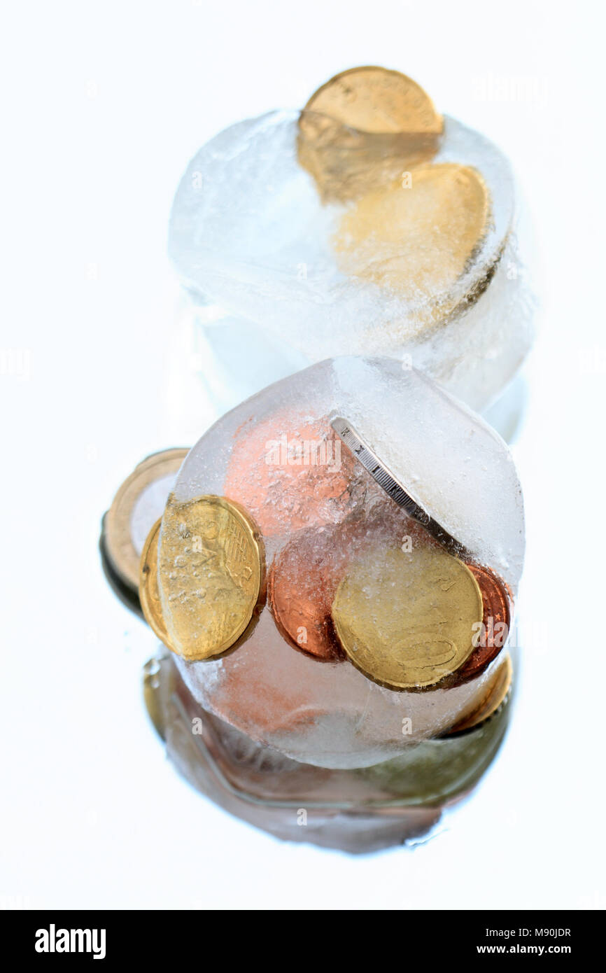 Monedas dentro de cubitos de hielo aislado sobre fondo azul. Foto de stock