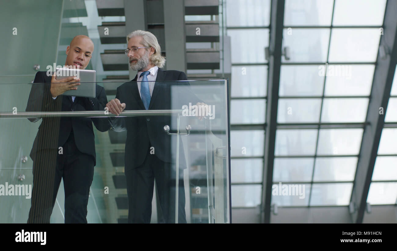 Latinos y caucásicos ejecutivos corporativos de pie en el segundo piso del edificio moderno hablar de negocio utilizando tablet digital. Foto de stock
