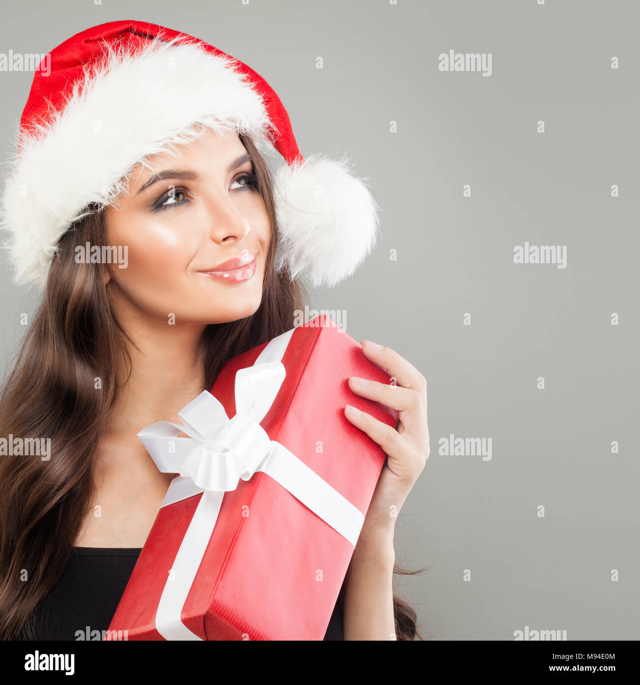 Navidad en Santa Mujer con sombrero rojo Caja de regalo de Navidad mirando hacia arriba sobre fondo gris. Concepto de Navidad o Año Nuevo Foto de stock