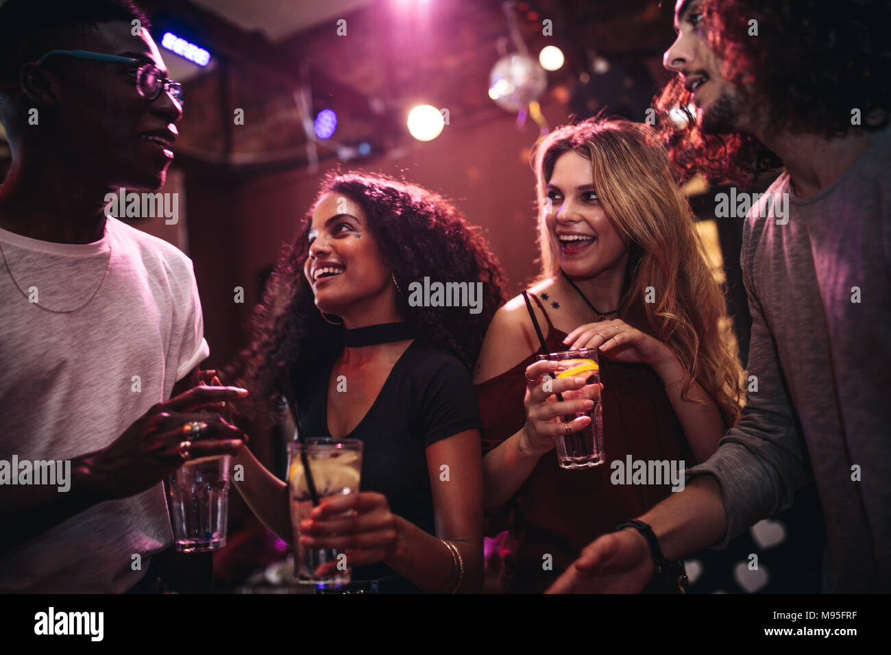 Diversos grupos de jóvenes con bebidas en un club. Hombres y mujeres felices disfrutando nightout en el bar. Foto de stock