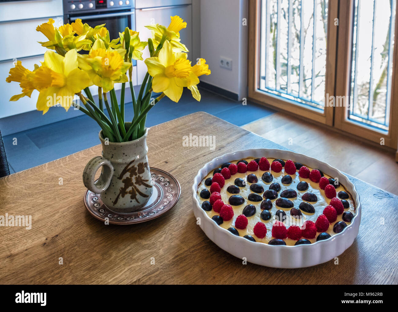 Deliciosa tarta de queso en el manjar blanco con uva & Berry puesta sobre  la mesa de madera con narcisos en un jarrón de cerámica Fotografía de stock  - Alamy