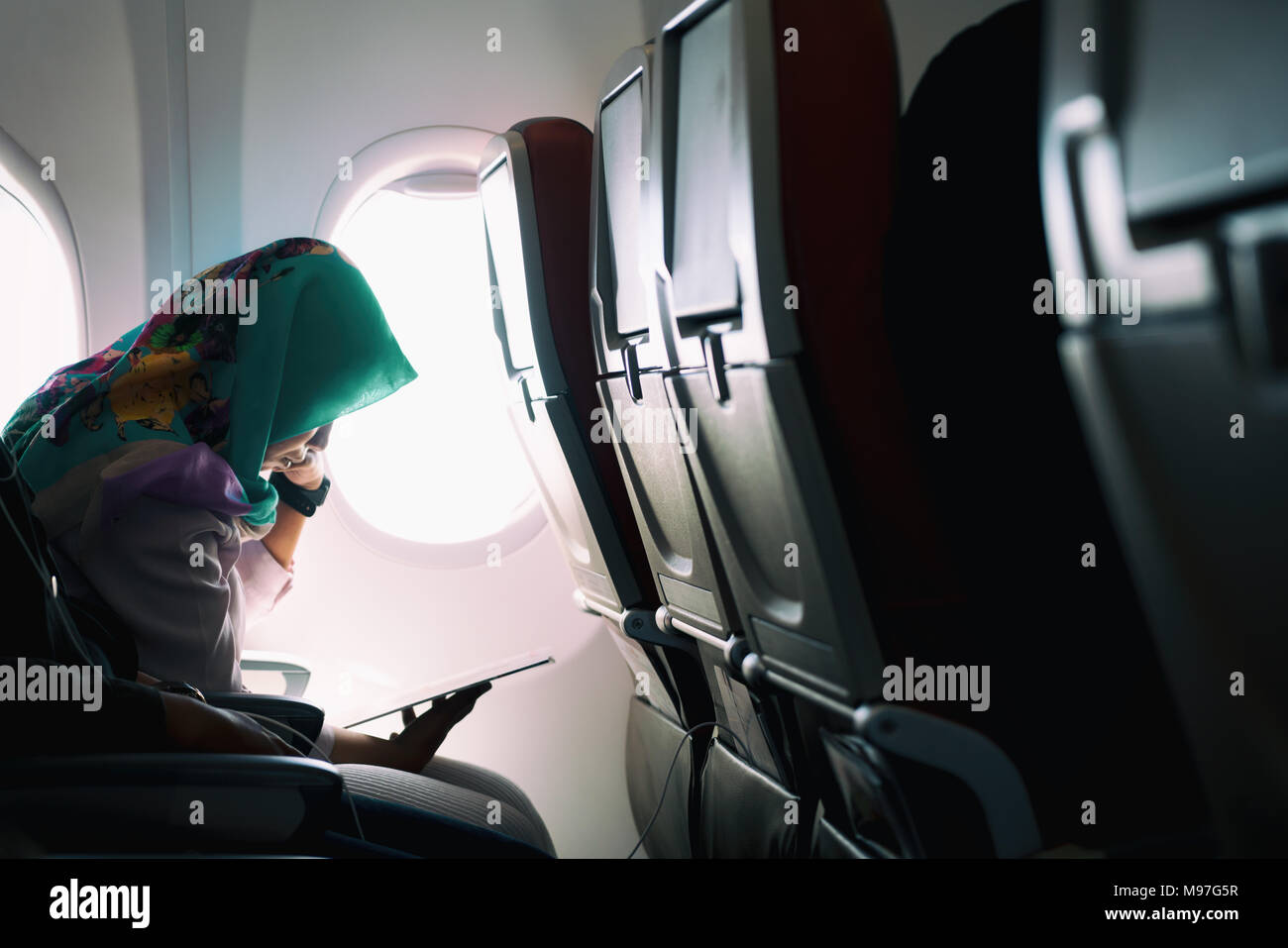 Mujeres Musulmanas solitaria viajando en avión, mientras que la lectura en asientos durante una puesta de sol, de modo ambiente de baja iluminación Foto de stock