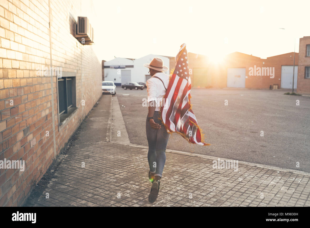 Vista posterior del joven corriendo con bandera americana a contraluz Foto de stock
