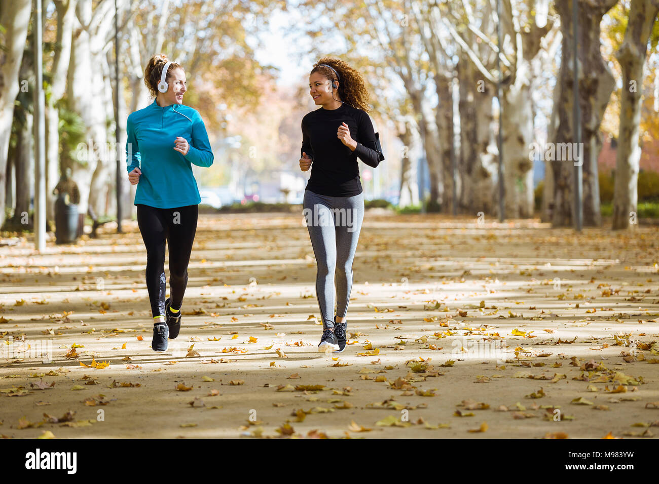Dos sonriente joven mujer corriendo en el parque escuchando música Foto de stock