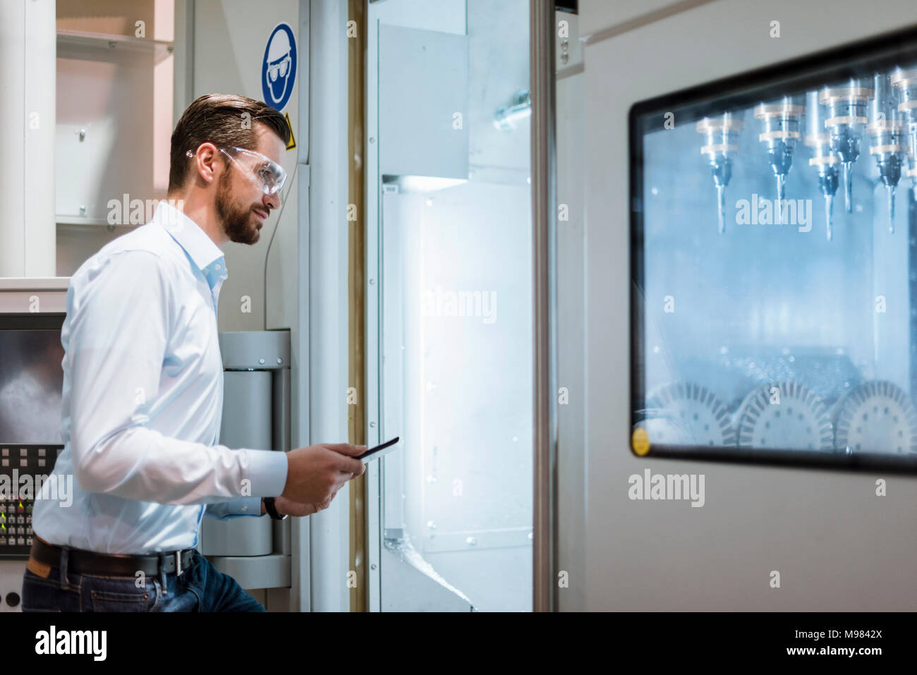 Empresario con tablet usando gafas de seguridad examinar la máquina en busca de fábrica Foto de stock