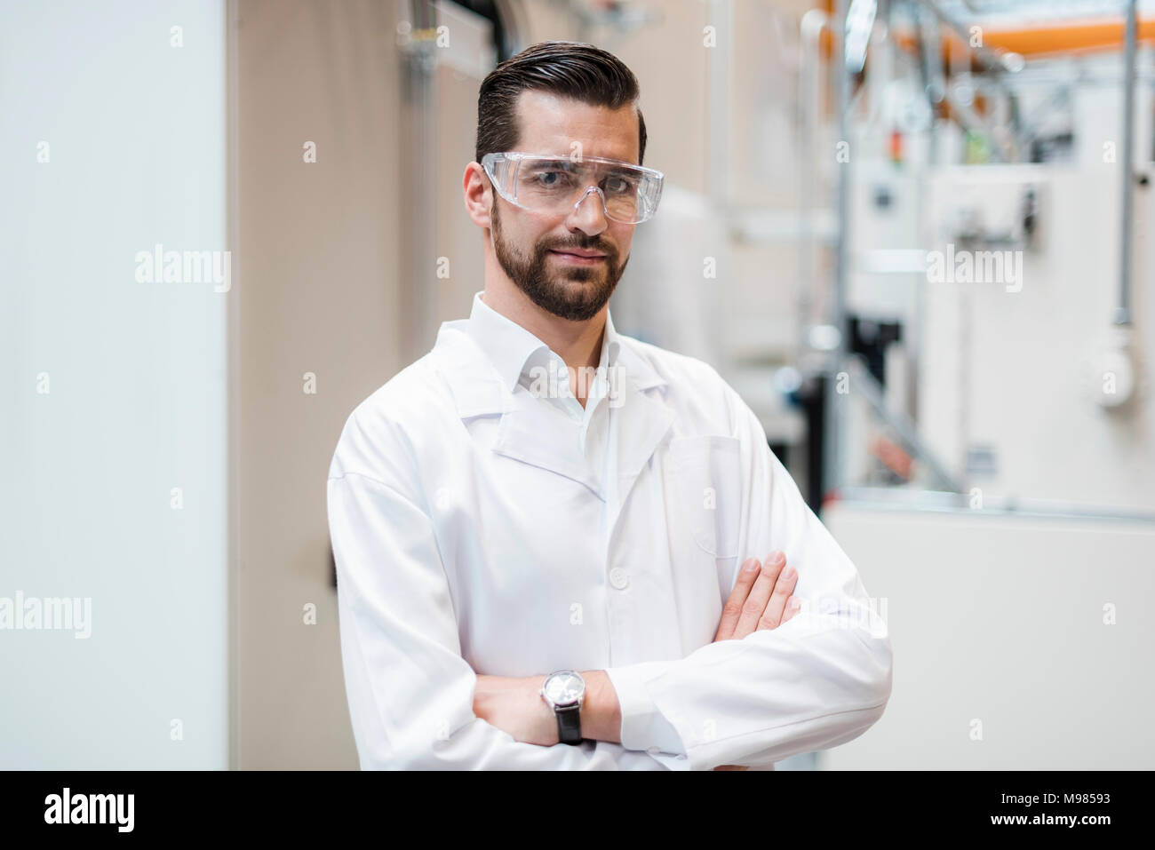 Retrato del hombre vestido con bata de laboratorio y gafas de seguridad en la fábrica. Foto de stock