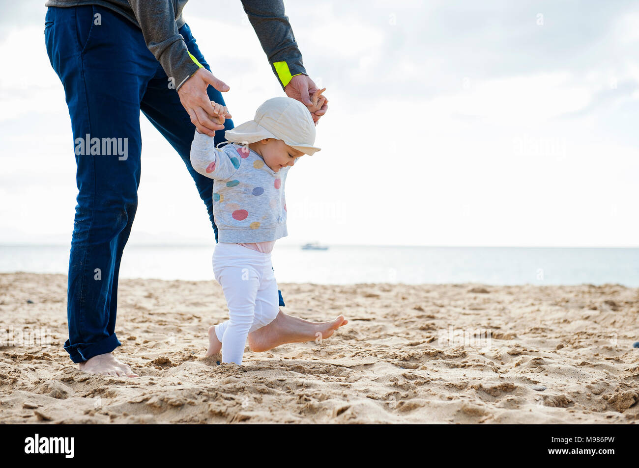 España, Lanzarote, niña caminando por la playa, con la ayuda de su padre. Foto de stock