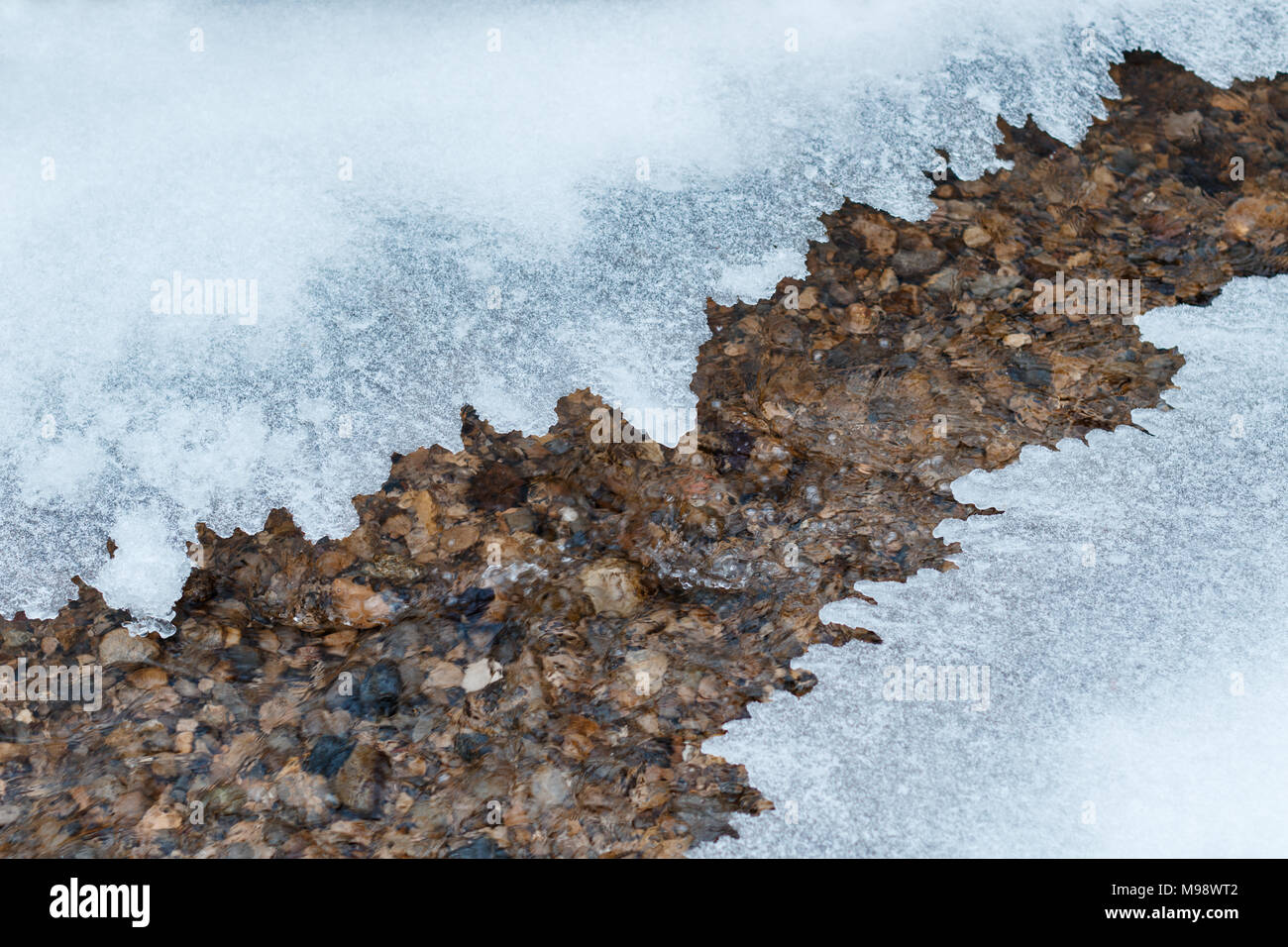 Placa delgada de hielo que cubre un pequeño arroyo de montaña Foto de stock