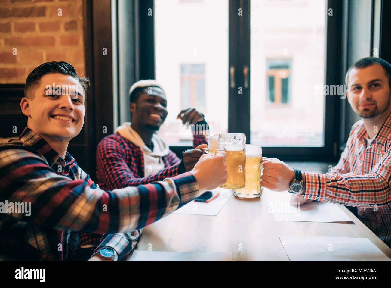 Grupo de jóvenes trabajadores de oficina tintineo feliz con cerveza en el pub, mirando, sonriendo. Foto de stock